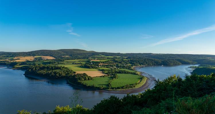 Vue panoramique d'un méandre de rivière avec des champs verts sous un ciel bleu clair.