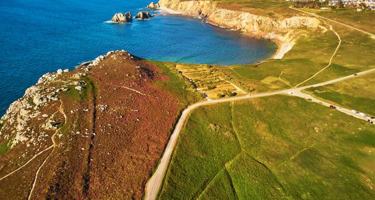 Vue aérienne d'un paysage côtier avec des falaises rocheuses et une route sinueuse.