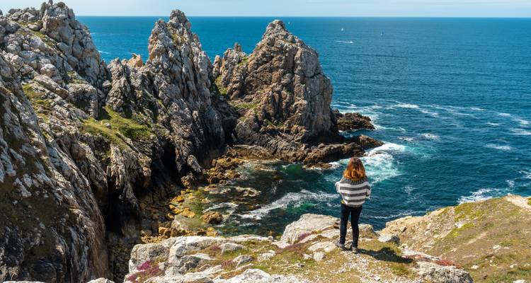 Personne debout au sommet de falaises rocheuses surplombant l'océan.