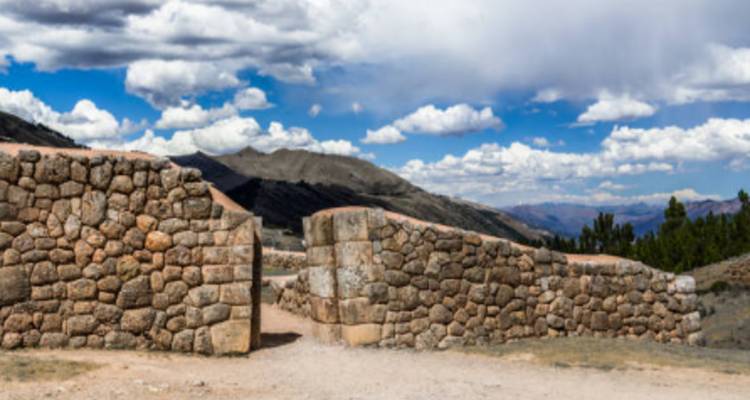 Antigua puerta de piedra con montañas y nubes en el fondo.