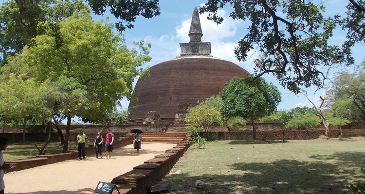 Stupa with people walking on a pathway in a green landscape.