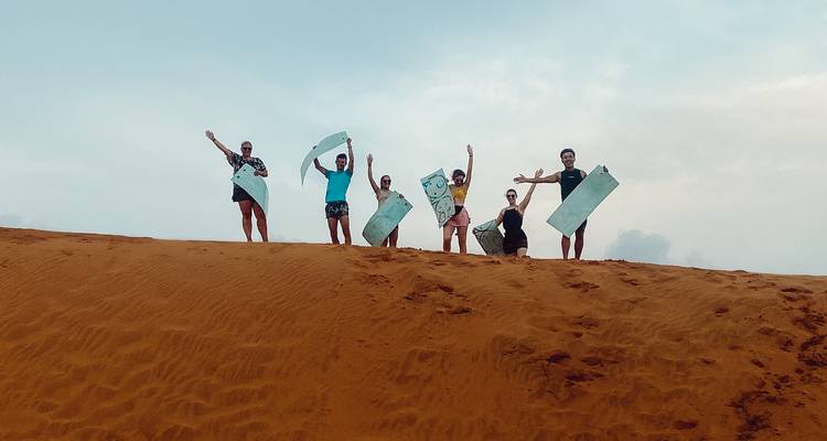Group posing on a sand dune with sandboards.