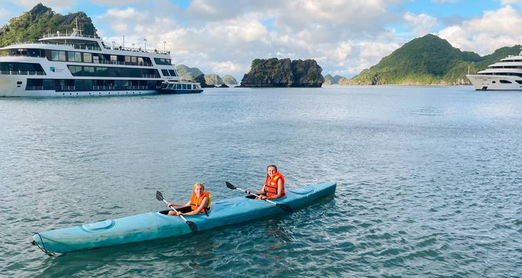 Two kayakers paddling in turquoise waters near limestone karsts.