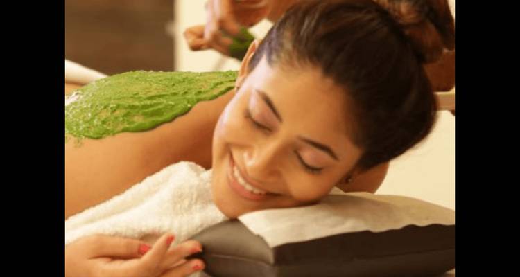 Woman receiving a massage with green herbal paste applied on her back.