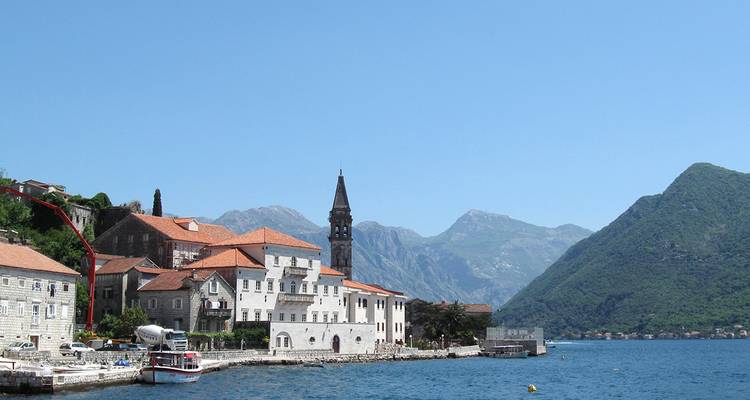 Pueblo costero con una torre de campana prominente y montañas.
