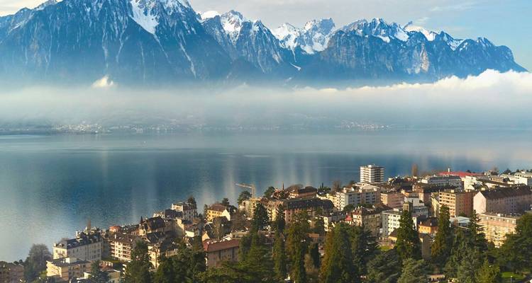 Montreux town on Lake Geneva framed by dramatic Alpine peaks and a layer of morning mist over the water.