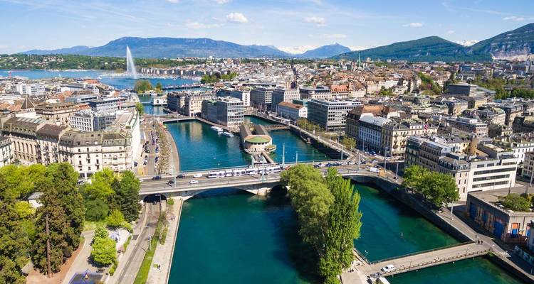 Aerial panorama of Geneva showing the Rhône River splitting the city, green parks and the distant Jet d’Eau fountain.