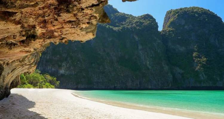 Pristine white-sand beach with turquoise water framed by dramatic limestone cliffs in southern Thailand.