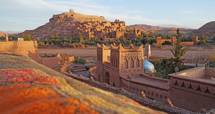 Panoramic view of the fortified adobe ksar of Ait Benhaddou atop a hill at sunset.