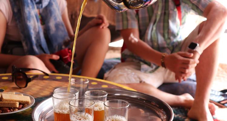 Traditional Moroccan mint tea being poured into glasses on a silver tray during a social break.