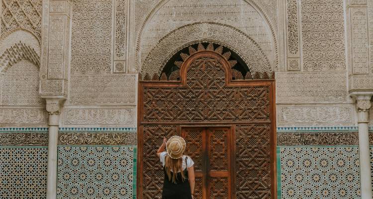 Traveler wearing a straw hat admiring an ornate wooden door and intricate mosaic tiles in Morocco.