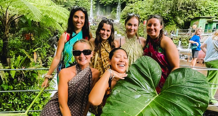 Group of women posing with a giant leaf at a rainforest attraction in Bali.