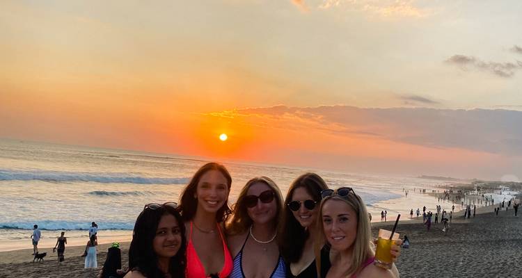 Group of friends posing on a beach at sunset with drinks.