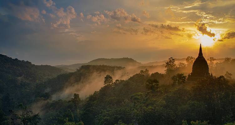 Een verre stupa op een heuvel te midden van een mistig panoramisch uitzicht bij zonsondergang.