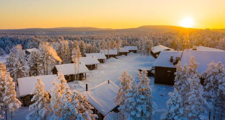 Lever de soleil d'hiver sur des cabanes enneigées dans la forêt.