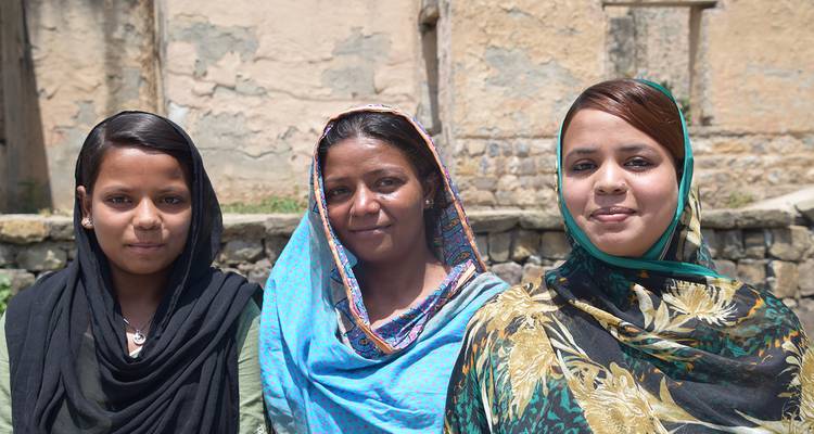 Trois femmes en vêtements traditionnels souriantes à la caméra.