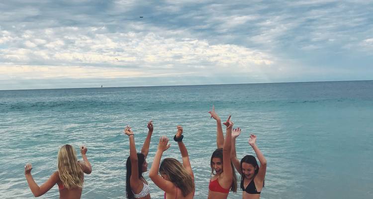 Tourists enjoying the beach, posing near the water with arms raised.
