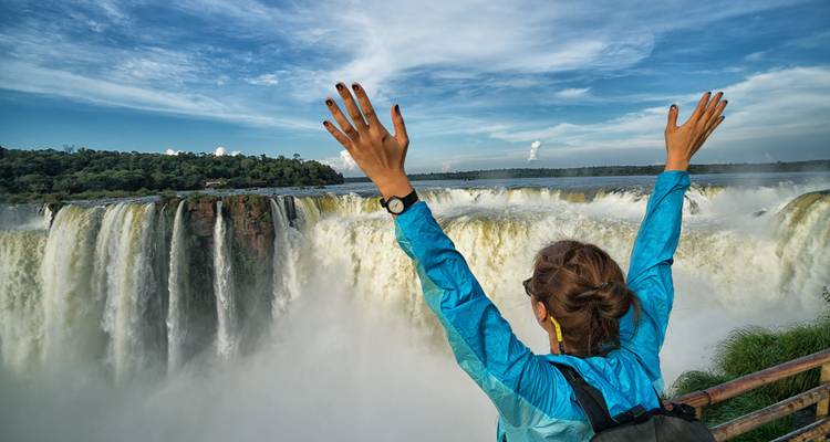 Person with arms raised in front of Iguazu Falls.