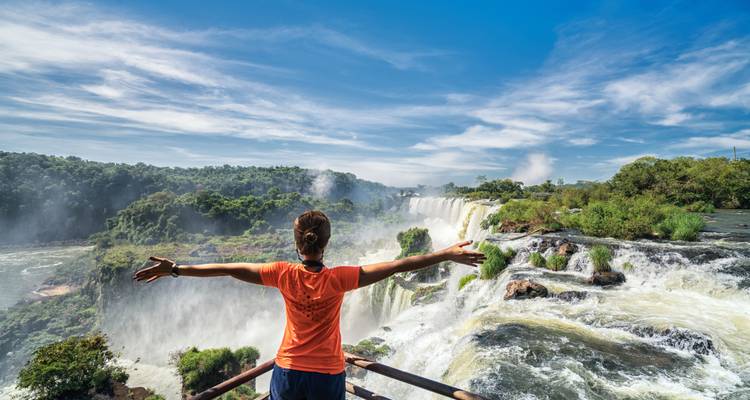 Person with arms outstretched in front of Iguazu Falls.