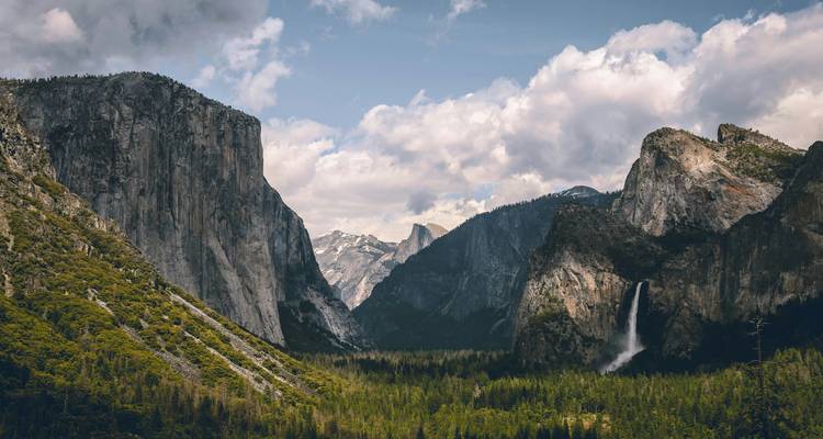 Klassiek uitzicht op Yosemite Valley met El Capitan, Half Dome in de verte en een waterval tussen beboste rotswanden