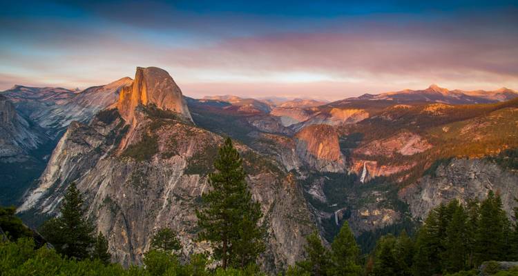 Half Dome en de omliggende granieten pieken van Yosemite gloeiend in golden hour licht boven het woud
