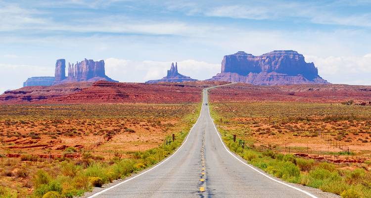Lange gerade Straße, die in eine Wüstenlandschaft mit Tafelbergen führt.