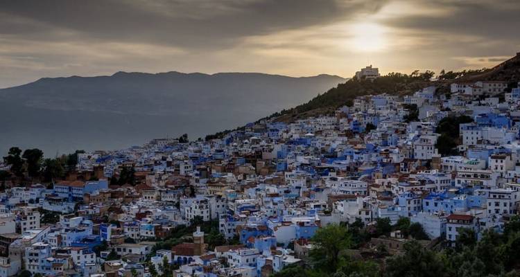 Paysage urbain de bâtiments bleus et blancs sur une colline au coucher du soleil.