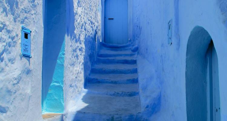 Escalier peint en bleu menant à une porte à Chefchaouen.