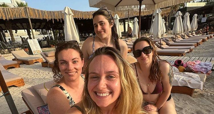 Selfie décontracté en bord de plage de quatre femmes se relaxant sur des transats sous des parasols sur une plage de sable.