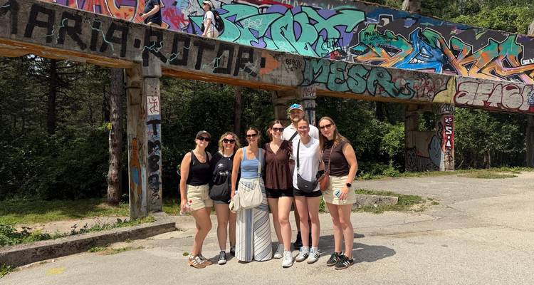 Groupe de voyageurs se tenant sous des graffitis colorés à la piste de bobsleigh olympique abandonnée de Sarajevo.