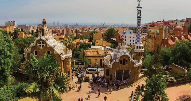 Colorful mosaic buildings and serpentine benches of Park Güell overlooking Barcelona cityscape.
