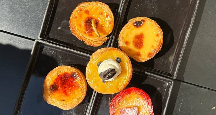 Five Portuguese custard tarts, some caramelised and topped, arranged on glossy black plates.
