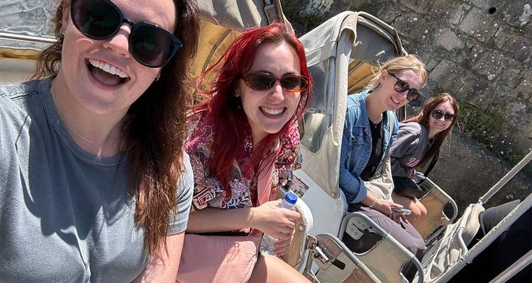 Four friends sit in open carriage seats laughing together on a sunny day