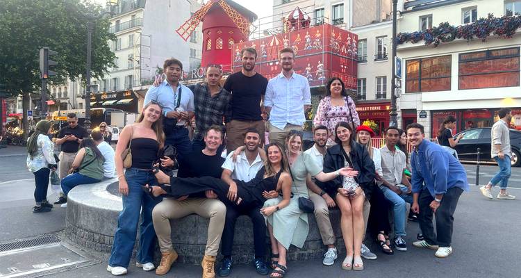 Large group of young travellers posing on a street near the red windmill of Moulin Rouge in Paris.