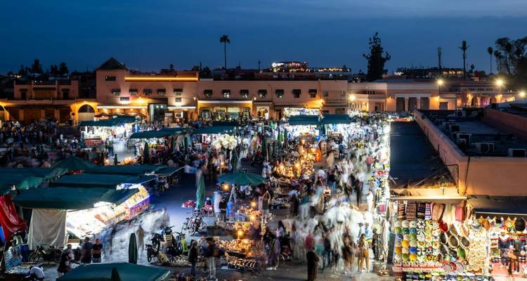 Scène de soirée d'un marché animé à Marrakech avec des lumières vives et des gens qui marchent.