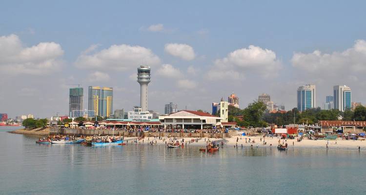 Coastal view of a busy beach with cityscape in the background.
