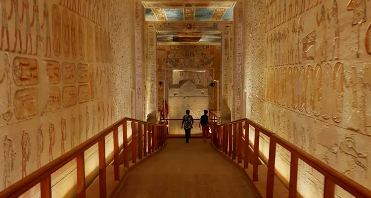 Intérieur d'un couloir de temple antique décoré d'hiéroglyphes, avec deux personnes qui marchent.