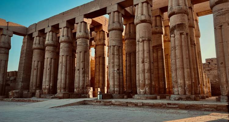 Rangées de colonnes de pierre dans un temple ancien avec un ciel bleu clair au-dessus.