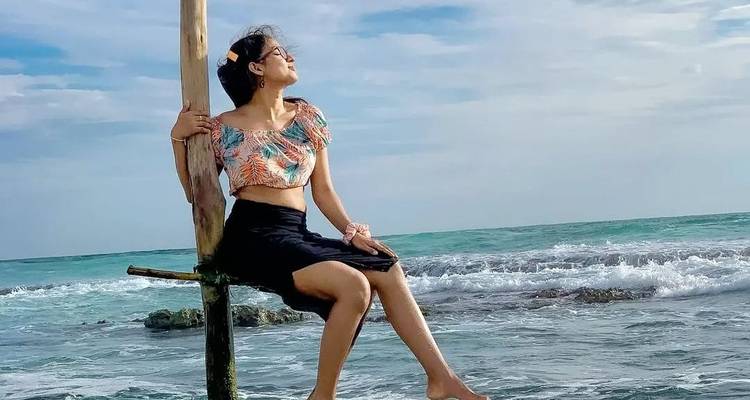 Femme assise sur un poteau dans l'océan avec des vagues en arrière-plan.