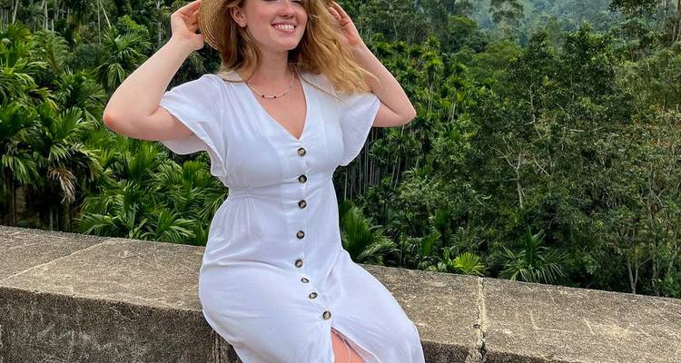 Femme assise sur un mur de pierre portant une robe avec un arrière-plan forestier.