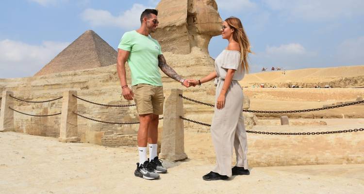 Couple holding hands in front of Sphinx and pyramids.
