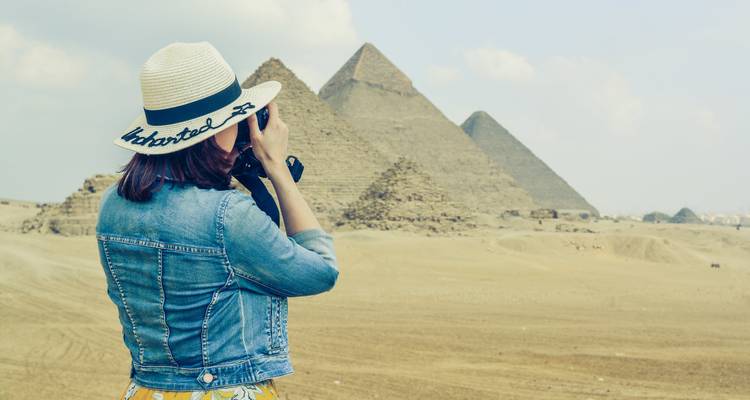 Woman photographing pyramids in desert landscape.