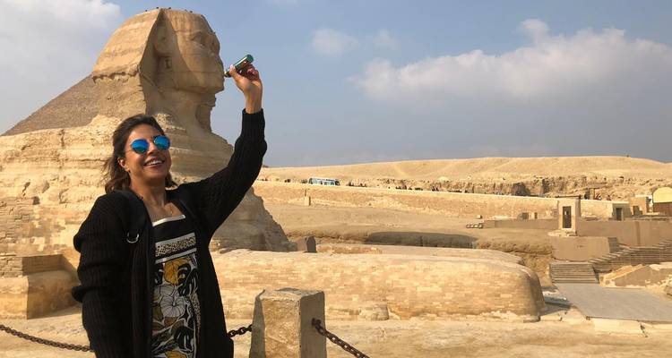 Woman playfully touching Sphinx in desert setting.