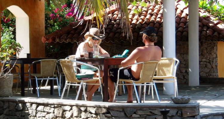 Deux personnes assises à un café en plein air avec du feuillage et une architecture rustique.