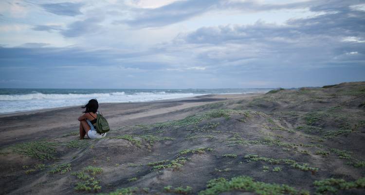 Personne assise sur une plage déserte avec de la végétation et des vagues.