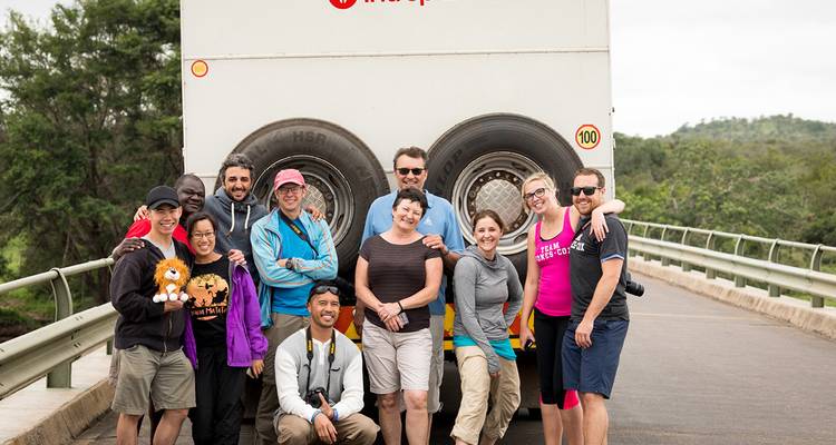 Group of people posing in front of a bus on a bridge.