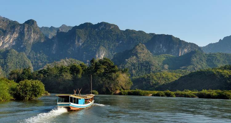 Un bateau traditionnel naviguant sur une rivière avec vue sur les montagnes.