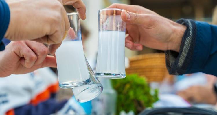Close-up of people clinking glasses filled with ouzo in a social setting.