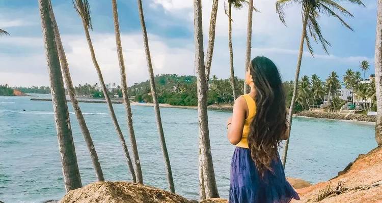 Femme regardant l'océan debout parmi les palmiers.