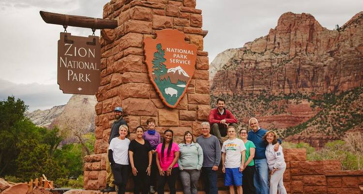Group of people posing by the Zion National Park entrance sign.